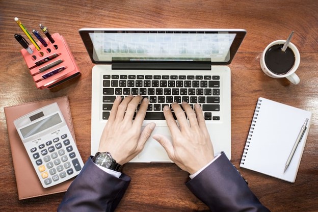 Business owner calculating virtual assistant cost on calculator and laptop - VOTG pricing guide