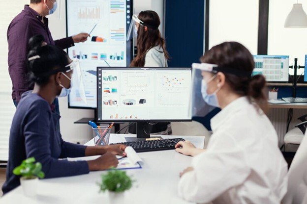 Multiethnic operations team analyzing business growth data on office monitors.
